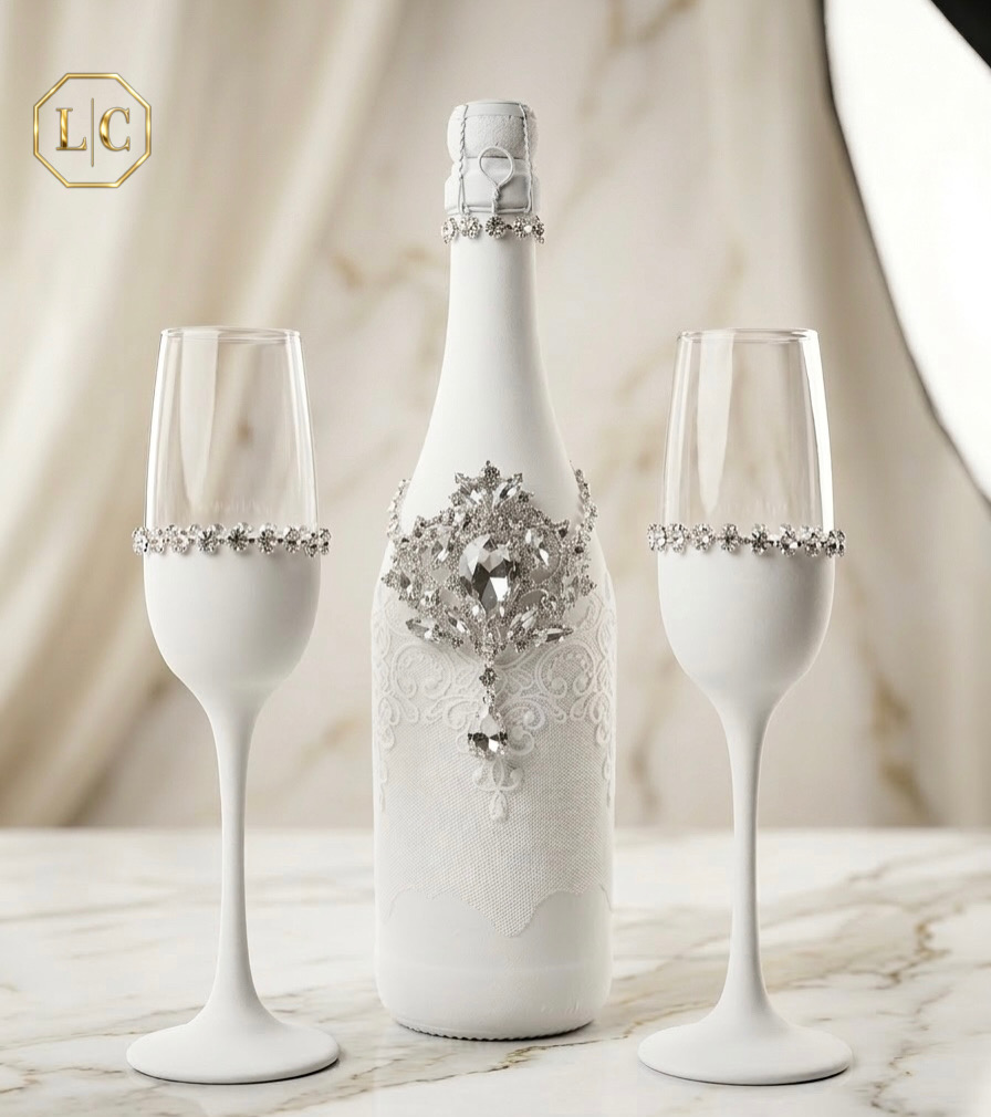 Botella blanca con encaje y cristal acompañada por dos copas para boda